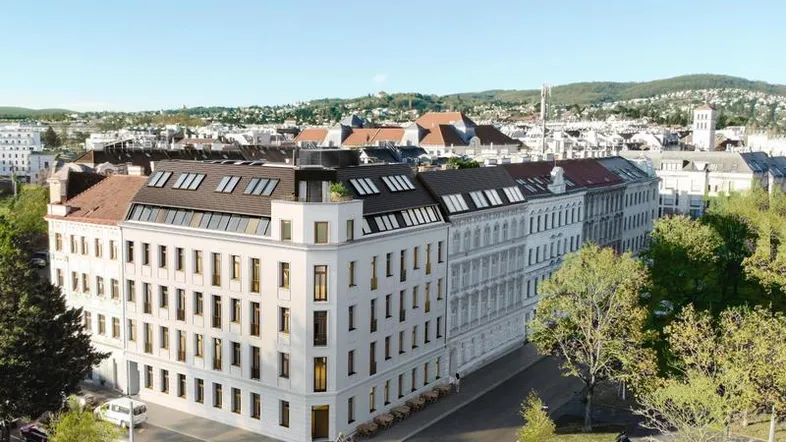 Luftaufnahme eines modernen Wohngebäudes in städtischer Umgebung mit grünen Hügeln im Hintergrund.