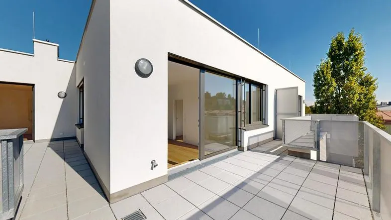 Geräumige Dachterrasse mit hellen Fliesen und Zugang zu den Innenräumen unter blauem Himmel.