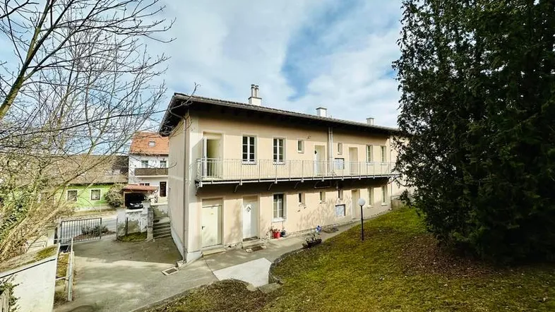 Mehrfamilienhaus mit mehreren Balkonen und einem gepflegten Vorgartenbereich.