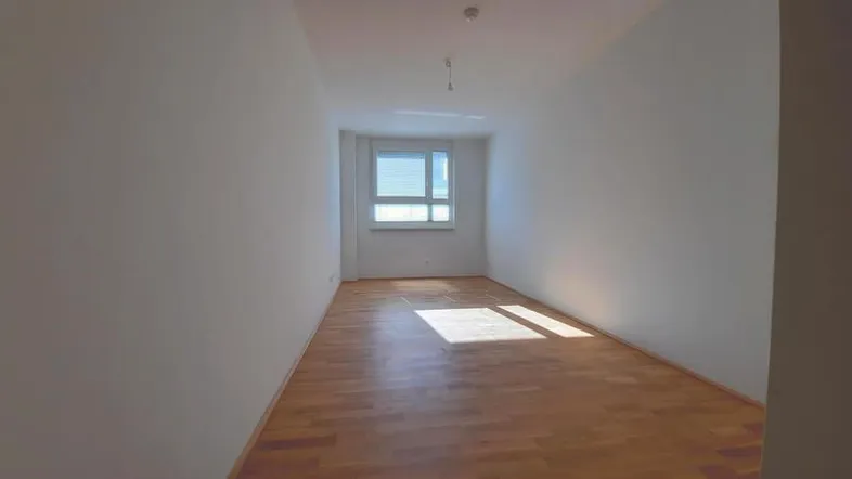 Helles, leeres Zimmer mit weißen Wänden und Holzboden, bereit zur individuellen Gestaltung.