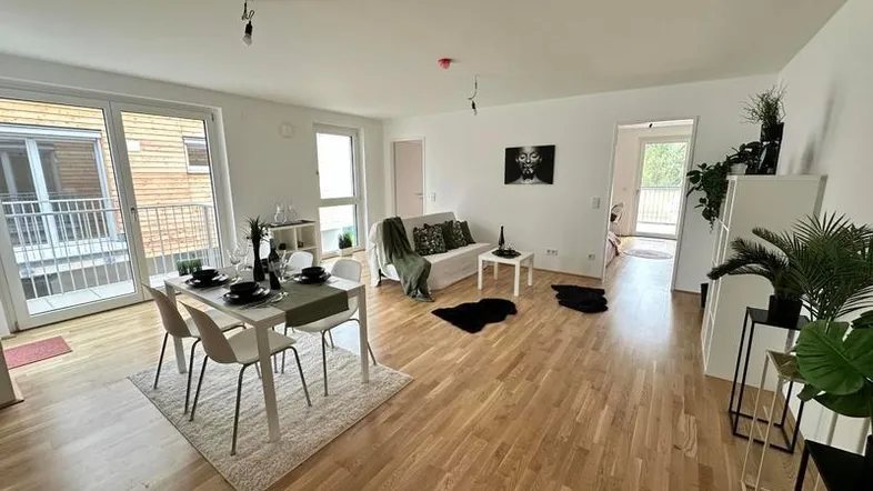 Heller offener Wohn-Essbereich mit Eichenparkett, Zugang zum Balkon und moderner Einrichtung.