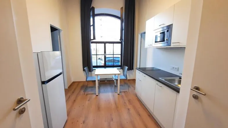 Kleine, funktionale Küche mit Kühlschrank, Mikrowelle und Essbereich am Fenster, ideal für Singles.