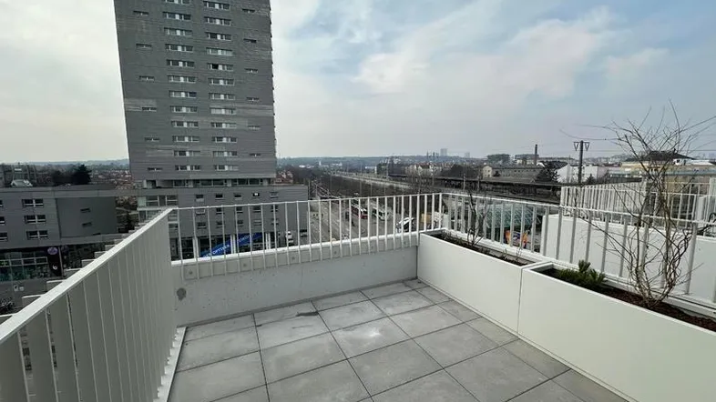 Geräumige Dachterrasse mit Fliesenboden, weißen Pflanzgefäßen und Blick auf die Stadt.