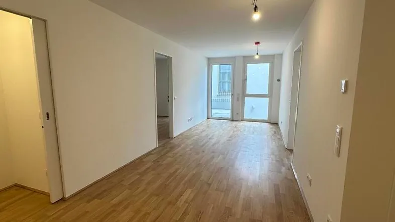 Helles Wohnzimmer mit Holzboden und Zugang zu einem Balkon oder einer Terrasse.