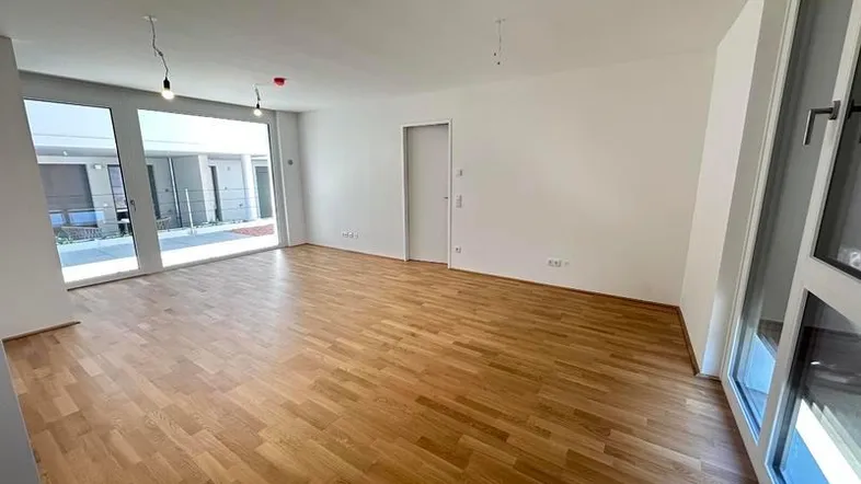 Helles Wohnzimmer mit Eichenparkett und großen Fenstern, die Zugang zum Außenbereich bieten.