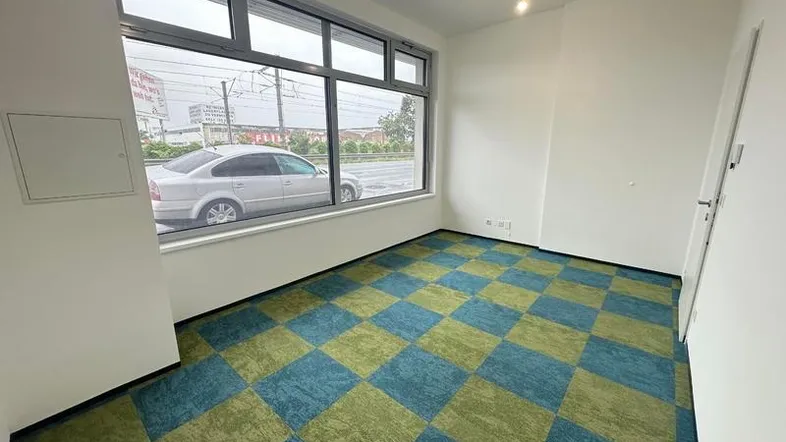 Heller Büroraum mit großen Fenstern zur Straße und einem auffälligen grün-blauen Teppichboden.
