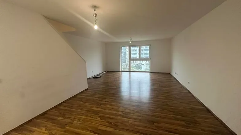 Geräumiges, leeres Wohnzimmer mit Laminatboden und Zugang zu einem Fenster mit Blick nach draußen.