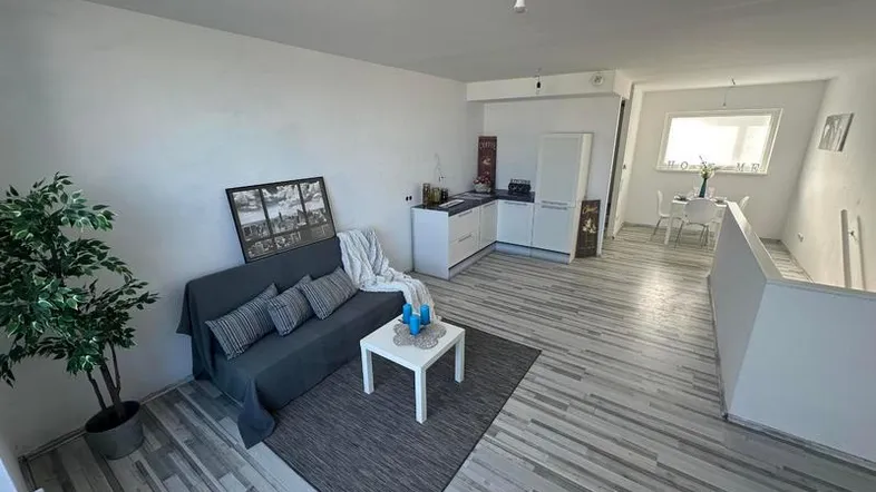 Heller offener Wohnbereich mit integrierter Küchenzeile, Sofa und Essbereich im Hintergrund.