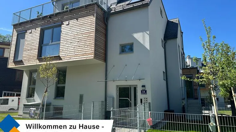 Modernes Mehrfamilienhaus mit Holzfassadenelementen und Balkonen in grüner Umgebung.