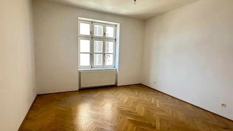 Helles Zimmer mit klassischem Fischgrätparkett und großem Fenster, bereit zur individuellen Gestaltung.