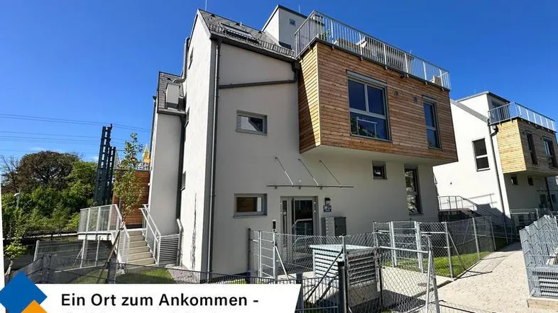 Modernes Gebäude mit weißer Fassade, Holzelementen und großen Fenstern unter blauem Himmel.