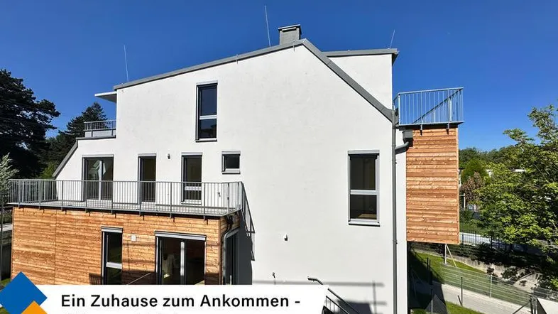 Moderne Wohnanlage mit weißer Fassade, Holzverkleidung und mehreren Balkonen unter blauem Himmel.