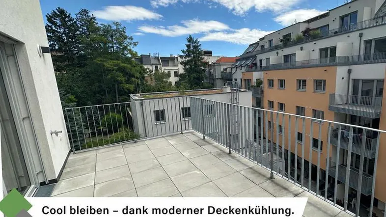 Große geflieste Terrasse mit Metallgeländer und Blick auf umliegende Gebäude und Bäume.