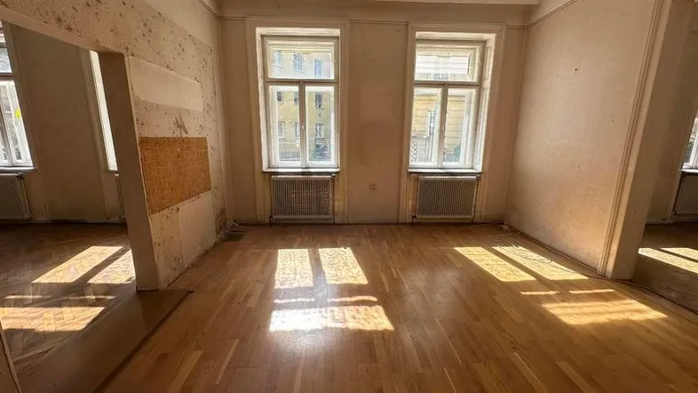 Helles Zimmer mit Holzboden und zwei Fenstern, bereit für Renovierung.