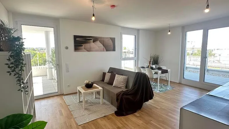 Helles Wohn- und Esszimmer mit Holzboden, Zugang zum Balkon und moderner Dekoration.