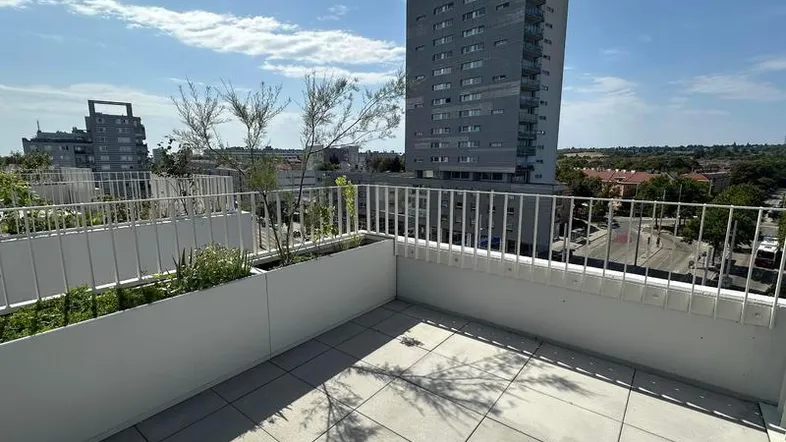 Helle Terrasse mit Fliesenboden, Pflanzenkübeln und Blick auf die Stadt.