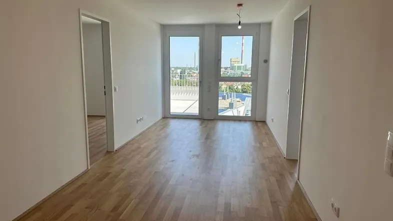 Helles Zimmer mit Parkettboden und Zugang zu einer Terrasse mit weitem Stadtblick.
