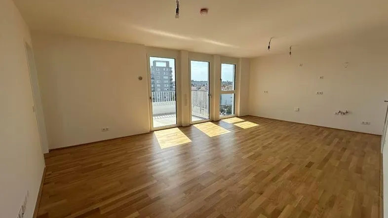 Helles, leeres Wohnzimmer mit Holzboden und Zugang zu einem Balkon, ideal für individuelle Gestaltung.