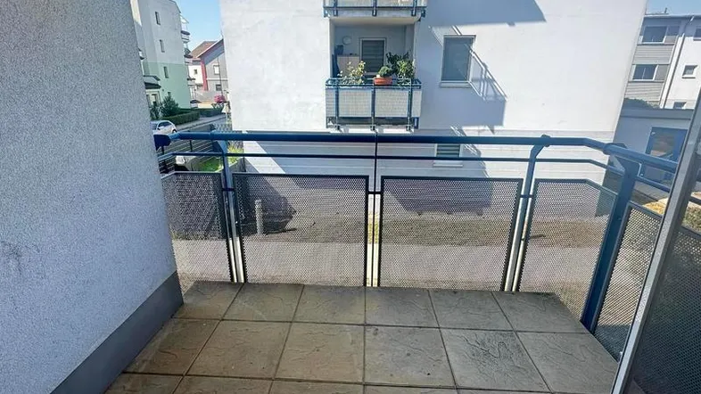 Heller Balkon mit Fliesenboden und Metallgeländer, bietet einen Blick auf die umliegenden Gebäude.
