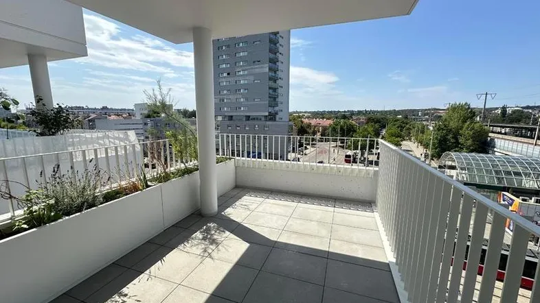 Geräumiger Balkon mit Fliesenboden, weißen Geländern und Blick auf die Stadt und umliegende Gebäude.