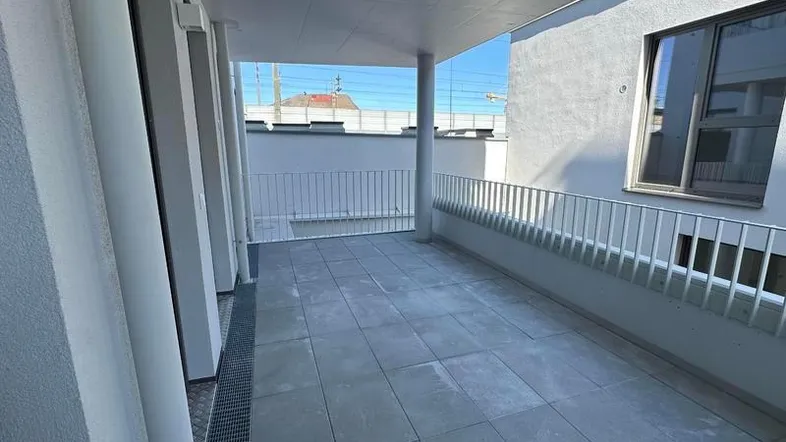 Überdachte Loggia mit Fliesenboden und weißem Geländer, ideal für entspannte Stunden im Freien.
