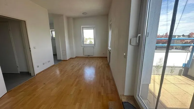Helles, leeres Zimmer mit Parkettboden und Zugang zu einem Balkon, ideal als Wohnbereich.