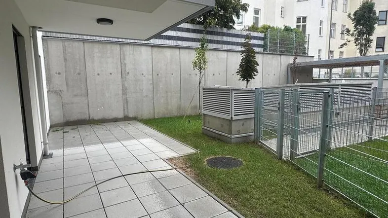 Gepflasterte Terrasse im Erdgeschoss mit Rasenfläche und einer hohen Betonwand.