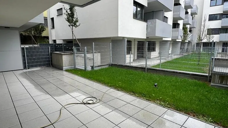 Gepflasterte Terrasse im Erdgeschoss mit Rasenfläche und Blick auf die moderne Wohnanlage.