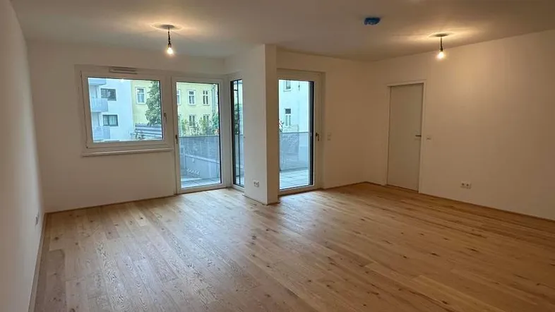 Heller, leerer Wohnraum mit neuem Holzparkettboden und Zugang zu einem Außenbereich.