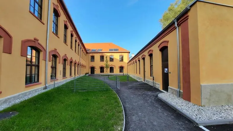 Neu renoviertes Gebäude mit gelber Fassade und gepflegtem Innenhof unter blauem Himmel.