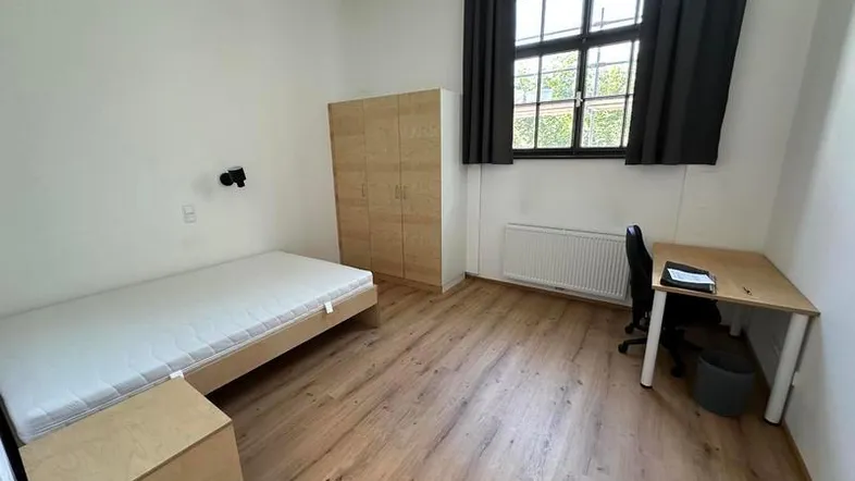 Helles Schlafzimmer mit Holzboden, großem Fenster und einfacher Möblierung für Studenten. Hohe Decken.
