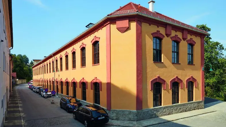 Historisches Gebäude mit gelber Fassade, roten Akzenten und Ziegeldach an einer Straße.