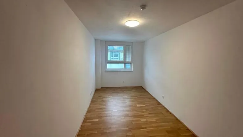 Leerer Raum mit Holzfußboden und einem Fenster, bereit zur individuellen Gestaltung.