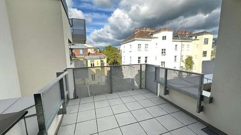 Geräumiger Balkon mit Fliesenboden und moderner Glasbrüstung, bietet Blick auf die umliegenden Gebäude.