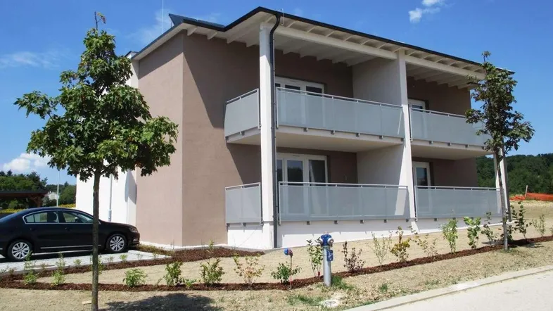 Modernes Mehrfamilienhaus mit Balkonen und neu angelegtem Vorgarten unter blauem Himmel.