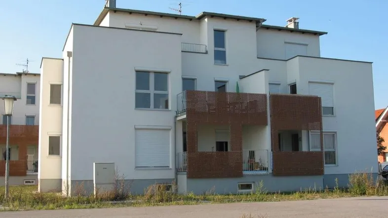 Modernes Mehrfamilienhaus mit weißer Fassade und mehreren Balkonen in ländlicher Umgebung.