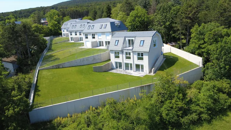 Neubau-Reihenhäuser in Hanglage mit großzügigen Gärten und Blick auf die bewaldeten Hügel.