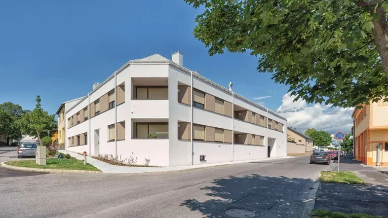 Modernes Eckgebäude mit weißer Fassade, Rollläden und integrierten Balkonen in städtischer Umgebung.