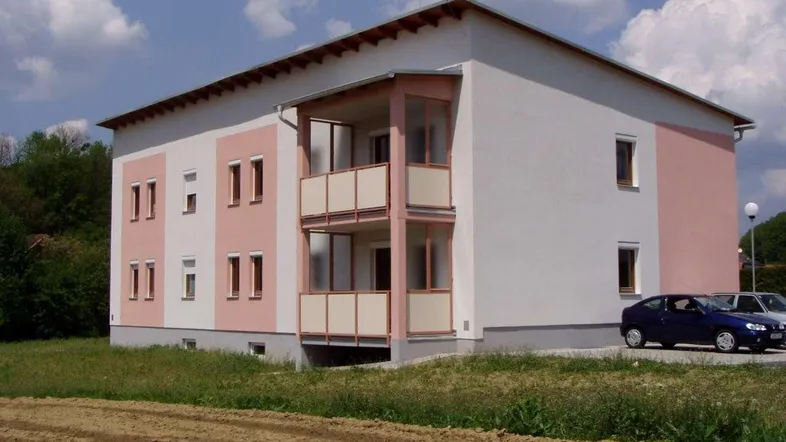 Neues Mehrfamilienhaus mit moderner Architektur, weiß-rosa Fassade, Balkonen und ländlichem Ausblick.