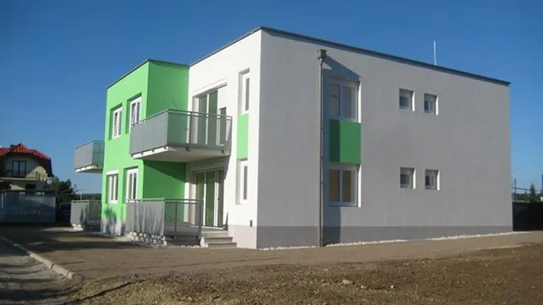 Modernes Mehrfamilienhaus mit grünen und grauen Fassaden, Balkonen und Flachdach in einem Neubaugebiet.