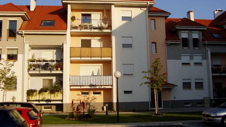 Mehrfamilienhaus mit roten Ziegeldächern, Balkonen und gepflegter Außenanlage bei Sonnenuntergang.
