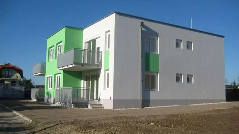 Modernes Mehrfamilienhaus mit flachem Dach, grünen und grauen Fassadenelementen sowie Balkonen.