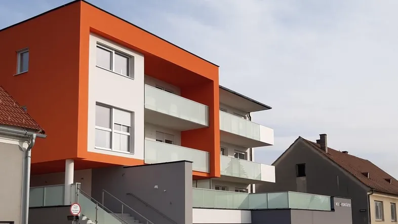 Modernes Gebäude mit auffälliger orange-weißer Fassade, Balkonen und Außentreppe unter klarem Himmel.