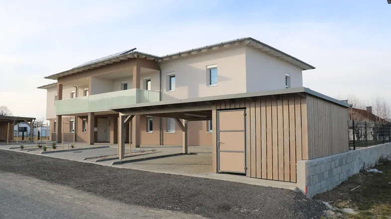 Modernes Neubau-Mehrfamilienhaus mit Carports, Abstellraum und Photovoltaikanlage auf dem Dach.