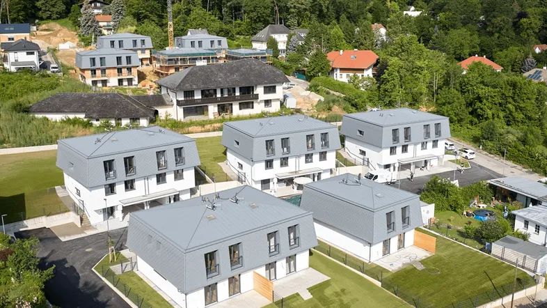 Luftaufnahme einer modernen Wohnsiedlung mit mehreren Häusern und grüner Umgebung am Waldrand.