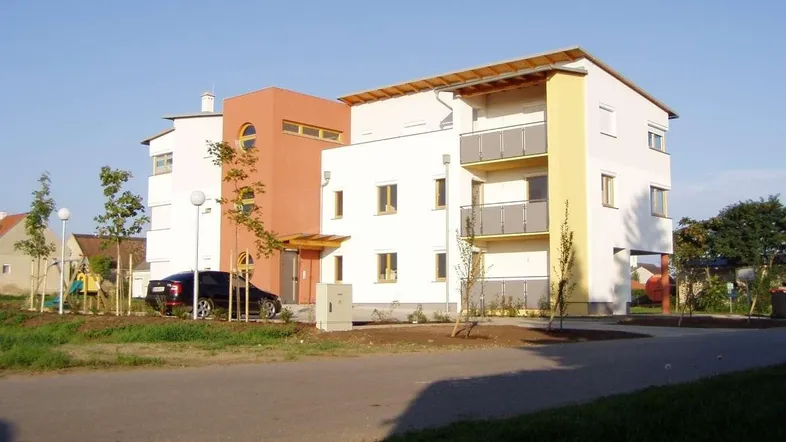 Modernes Mehrfamilienhaus mit farbiger Fassade, Balkonen und gepflegter Außenanlage.