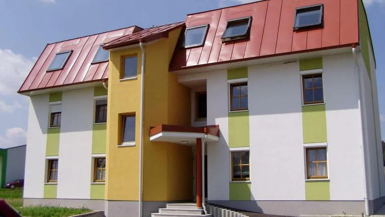 Modernes Mehrfamilienhaus mit farbiger Fassade, Satteldach und Dachfenstern in grüner Umgebung.