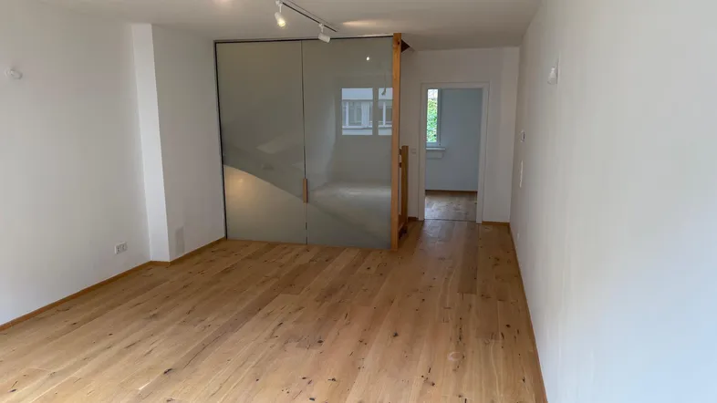 Helles Zimmer mit Holzboden und moderner Glastrennwand, ideal als Wohn- oder Arbeitsbereich.