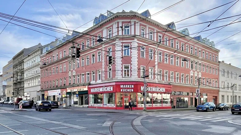 Eckgebäude mit roter Fassade und Geschäften im Erdgeschoss an einer belebten Kreuzung.