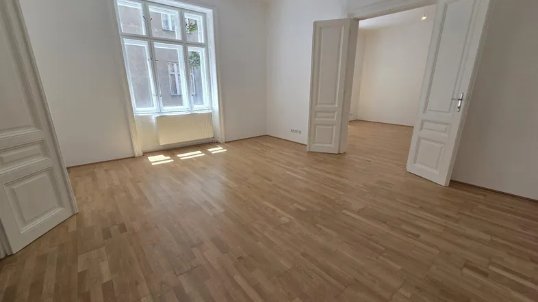 Helles, leeres Zimmer mit Parkettboden und hohen Türen, das vielseitig nutzbar ist.